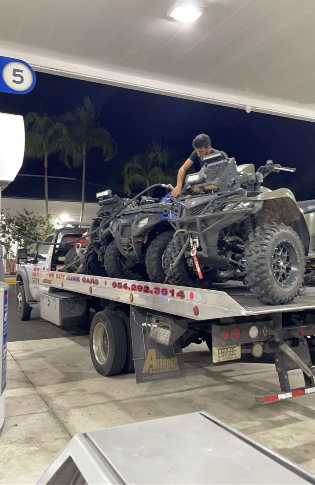 ATVs loaded on a flatbed tow truck at a gas station at night