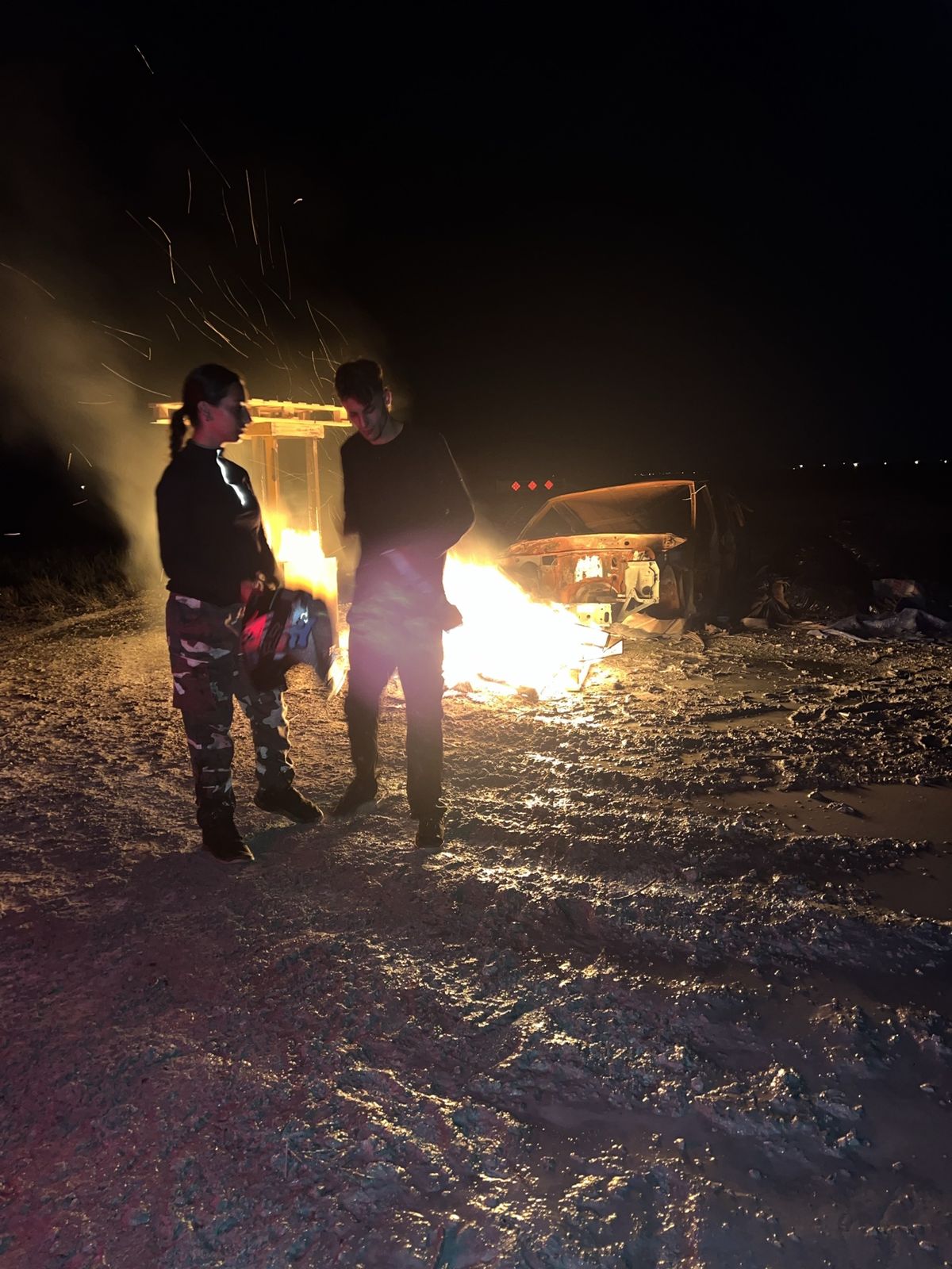 Two riders by a bonfire on a muddy trail at night