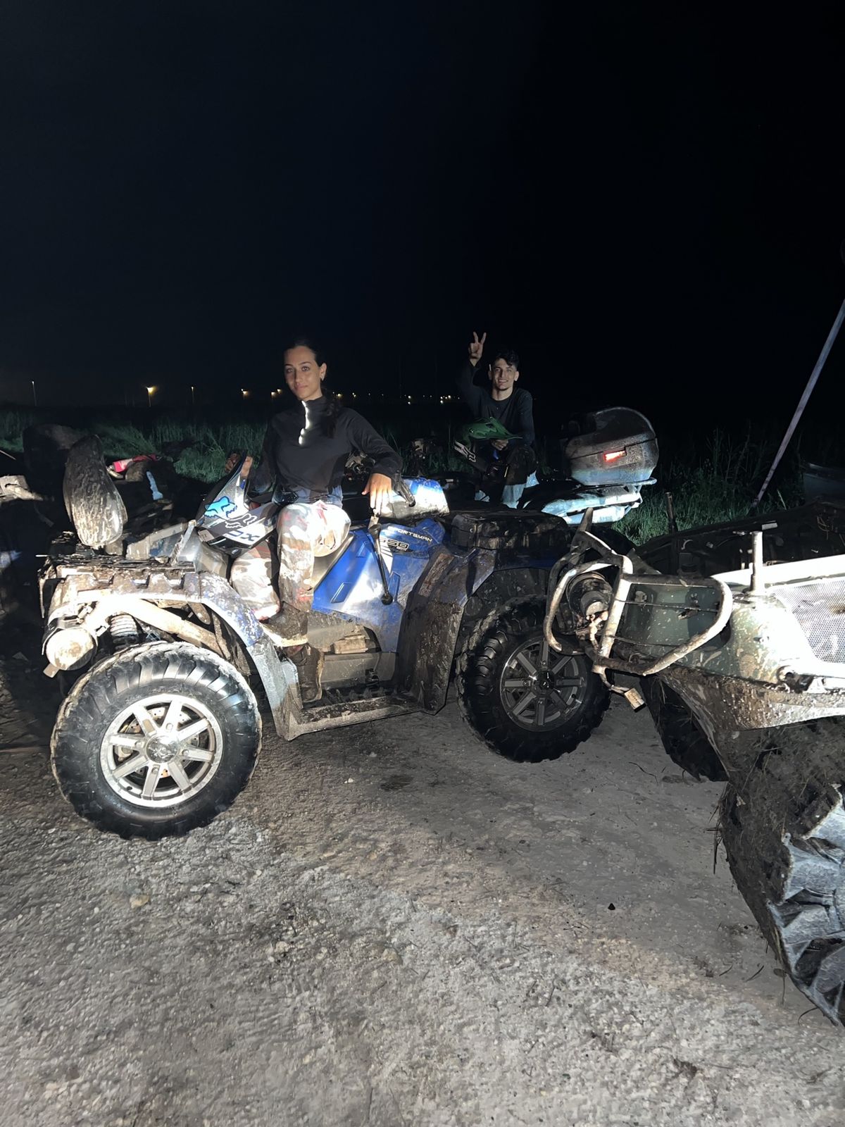 Woman on a blue ATV with a friend giving a peace sign at night