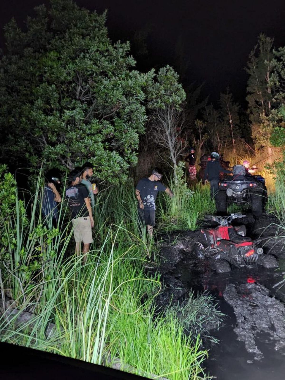 Group of riders around ATVs stuck in deep mud at night