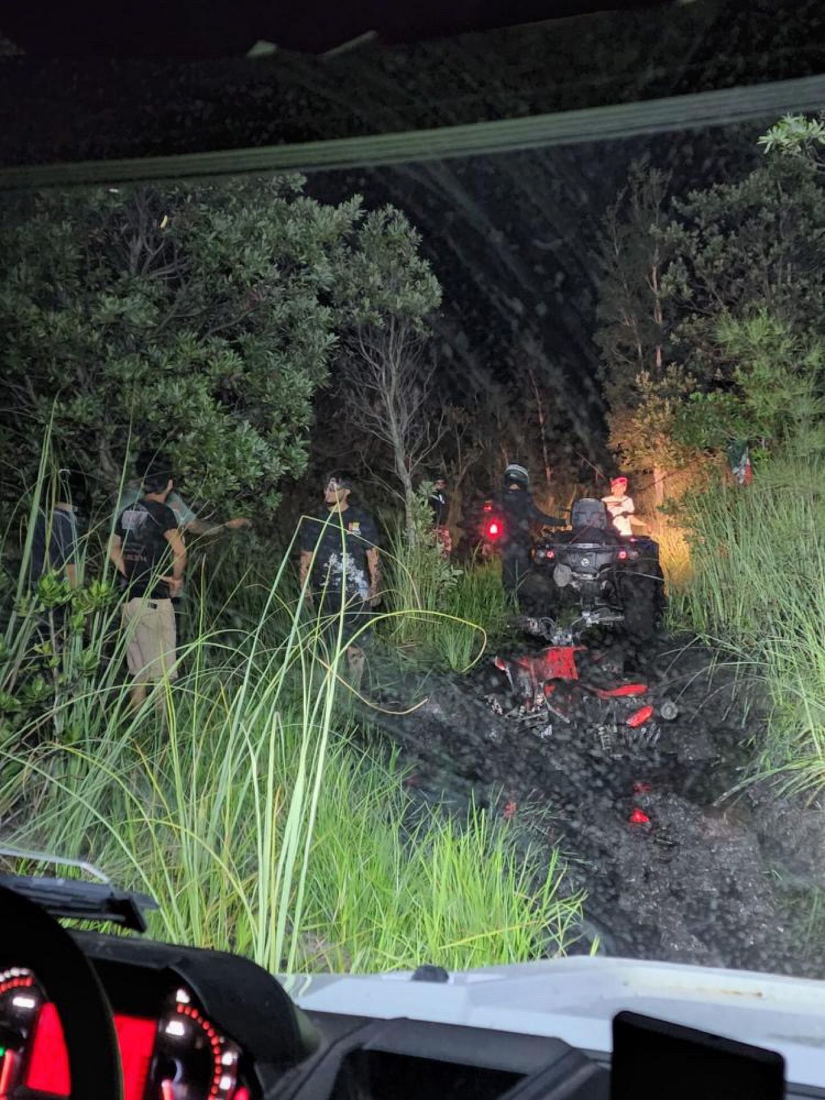 Riders gathered around ATVs in the mud at night