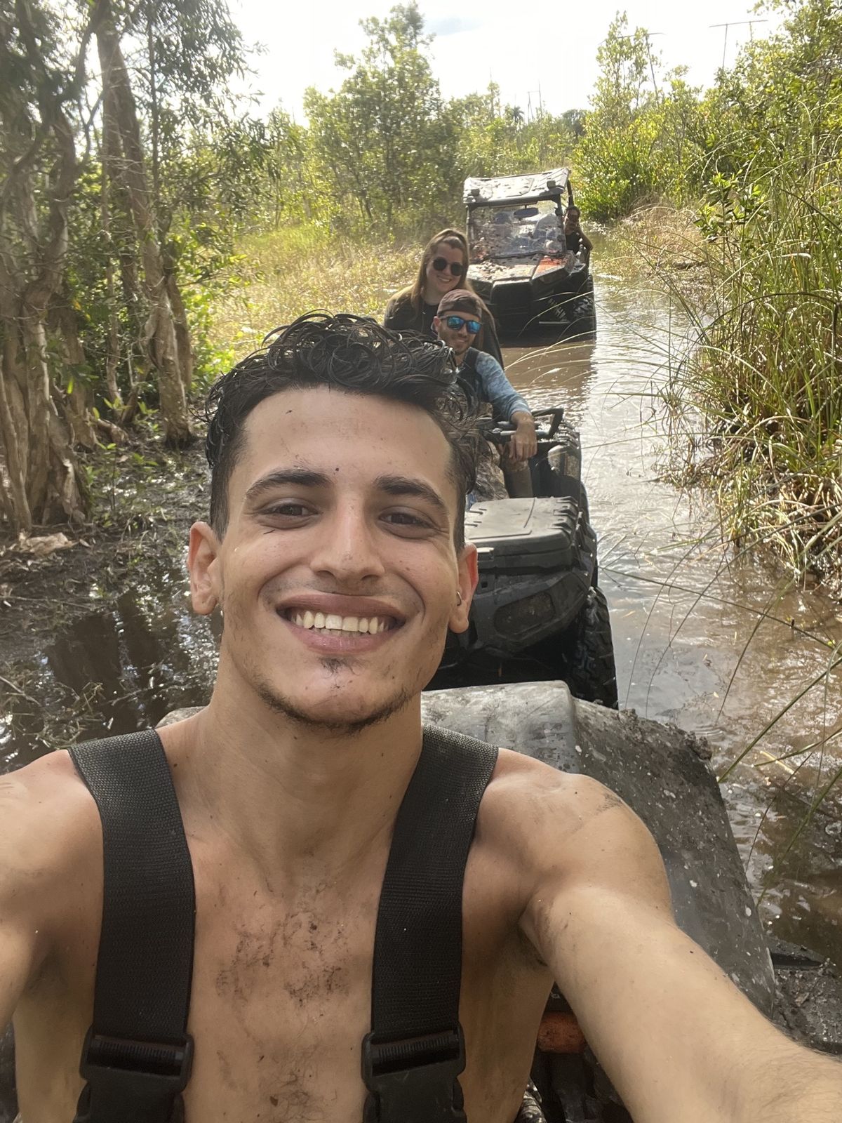 Rider selfie on an ATV in a water trail with friends behind