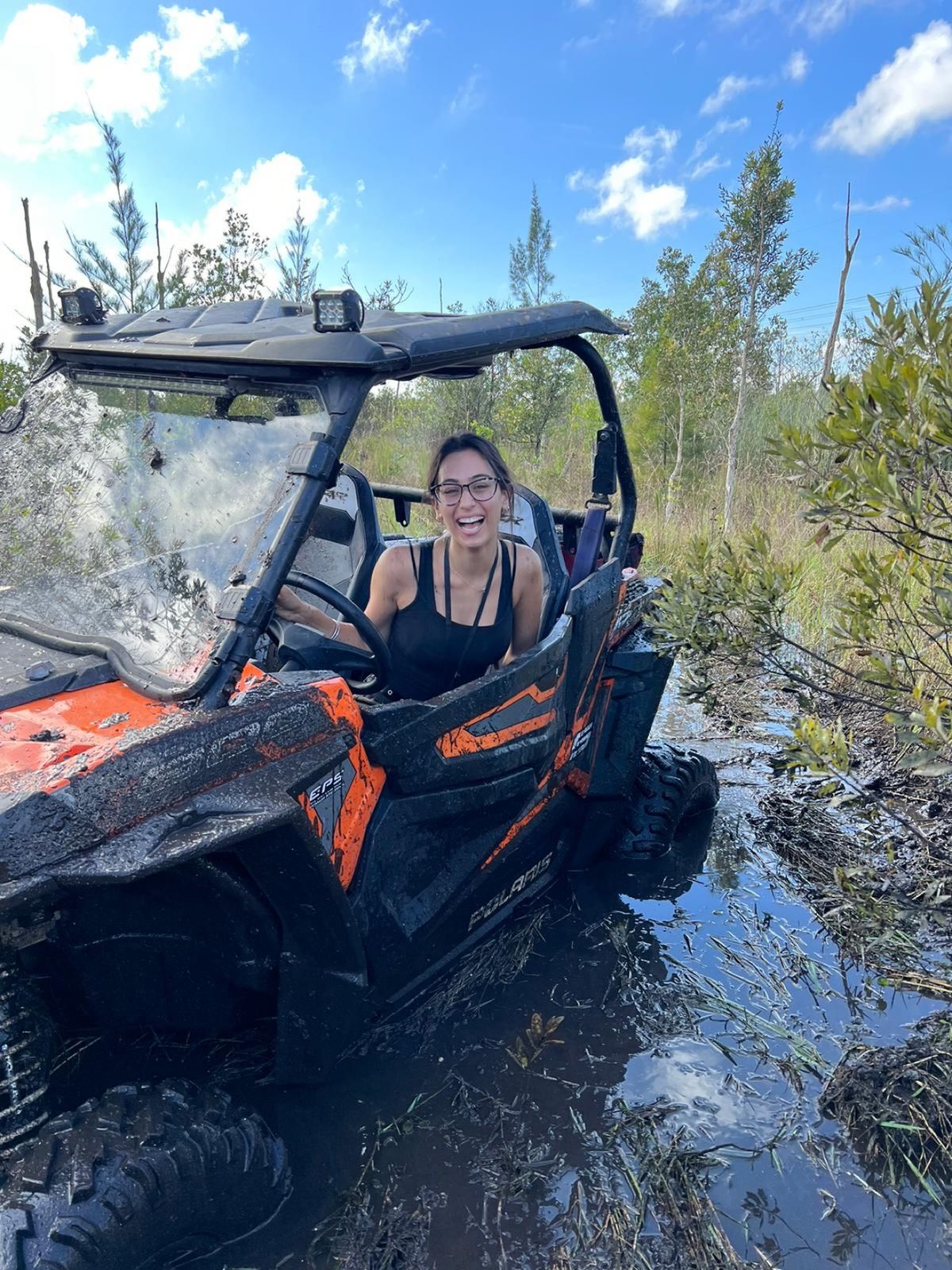 Woman driving an orange SXS through deep mud