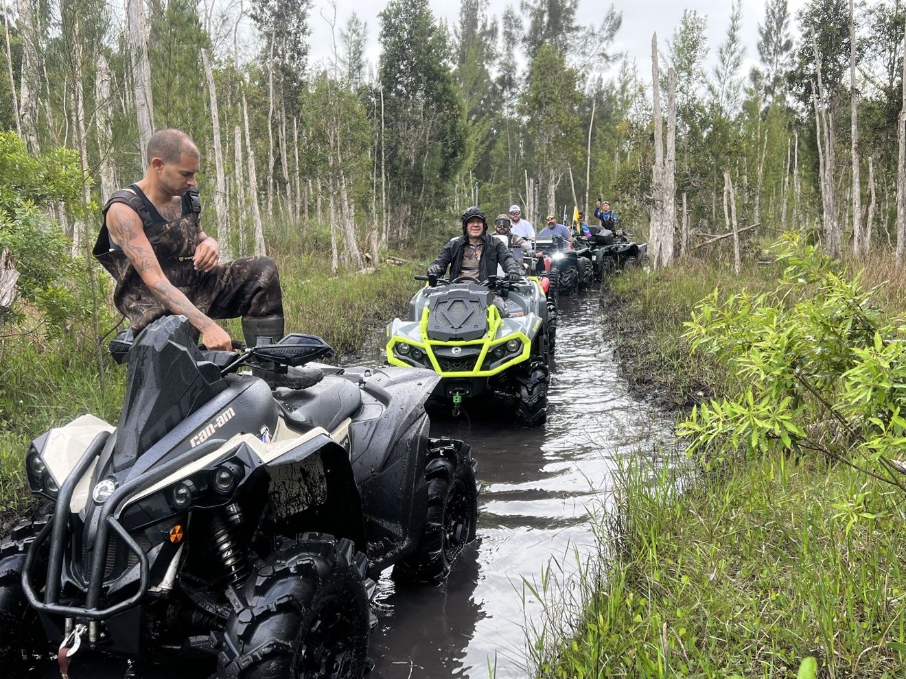 Riders on ATVs in a flooded woods trail