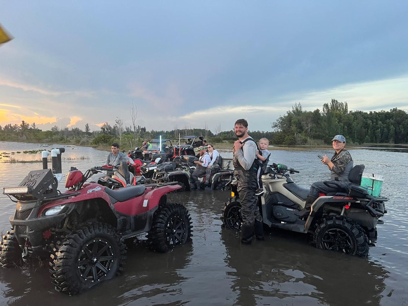 Group of riders and ATVs in the water at sunset