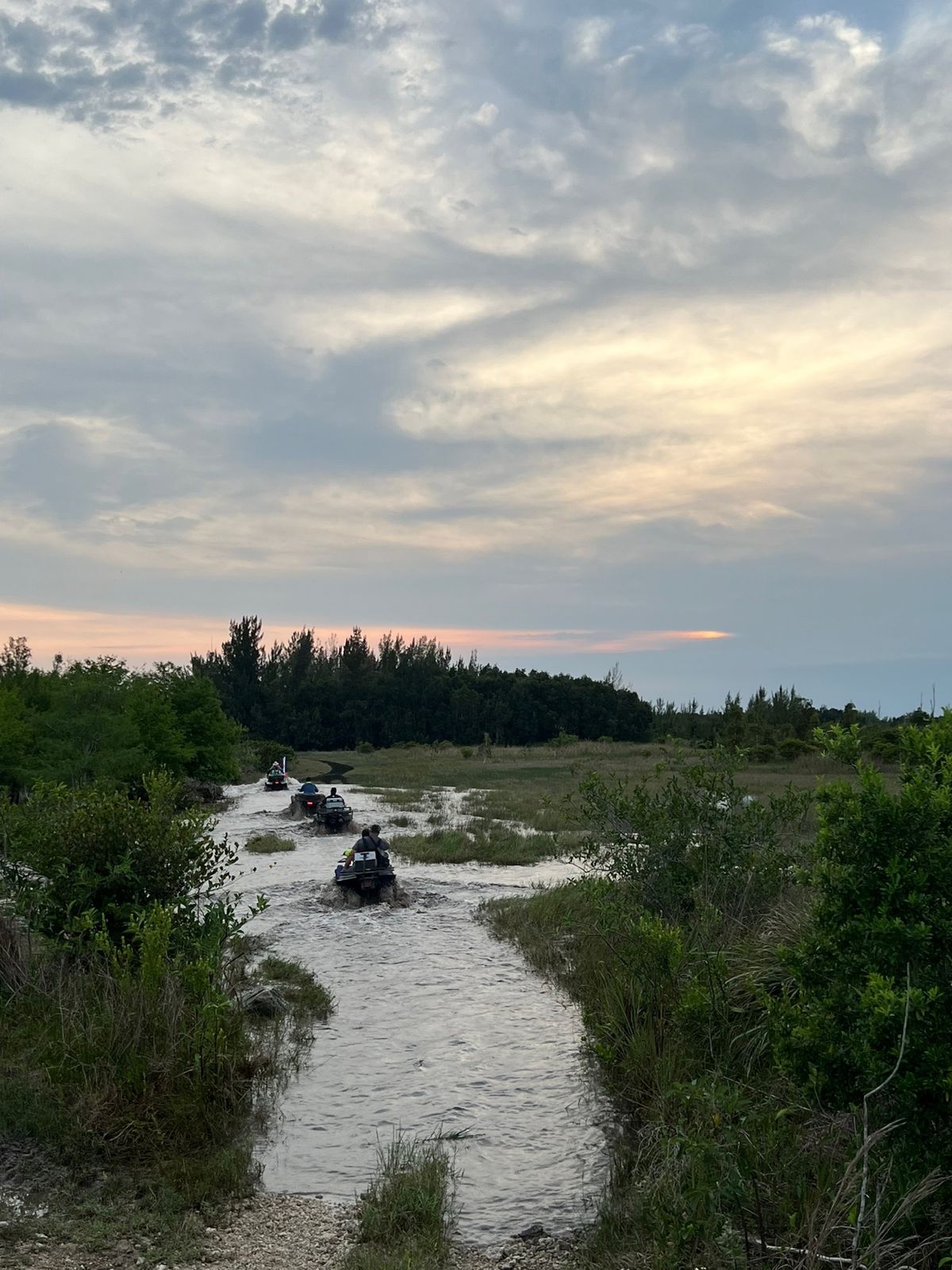 ATVs riding through a flooded trail at sunset