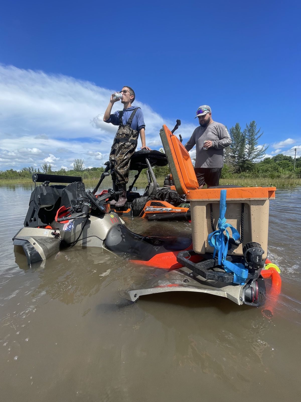 Riders on ATVs in deep water with a cooler